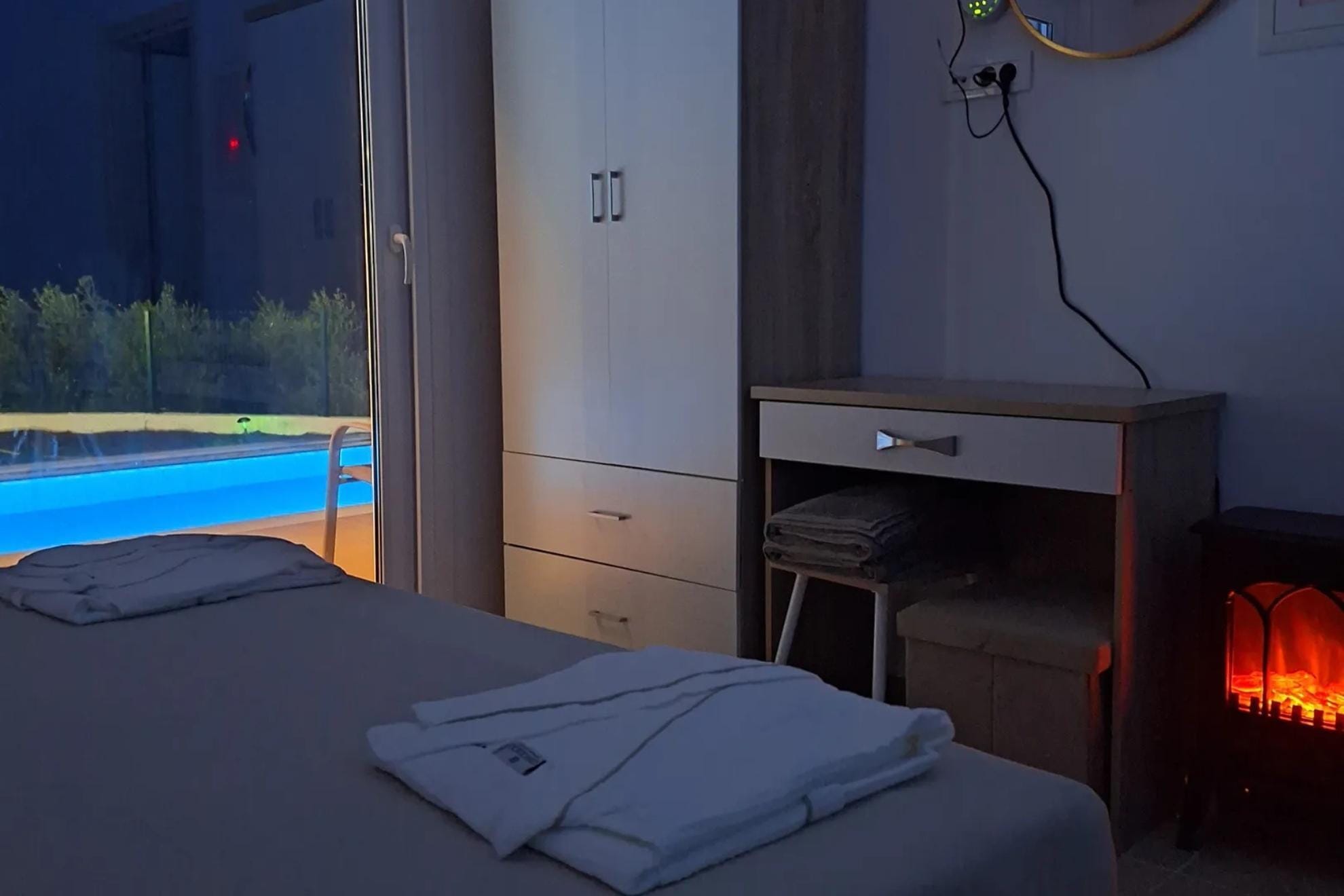 Room with bed, balcony, fireplace and pool view at night